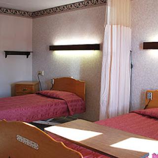 A simple hotel room featuring two twin beds with pink bedding and soft lighting.