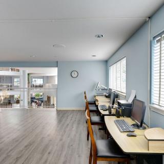 A modern office workspace with desks, computers, and chairs along a windowed wall.