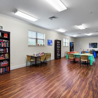 A classroom with tables, chairs, and bookshelves on a hardwood floor.