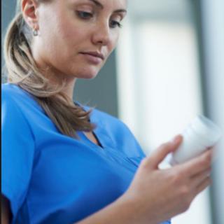 A healthcare professional in a blue uniform examines a bottle.