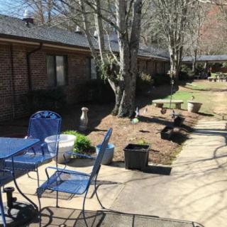 A sunny patio area with chairs, tables, and potted plants along a walkway.