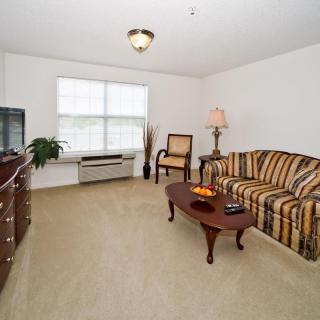 A cozy living room with a striped sofa, wooden coffee table, armchair, and a television under a large window.