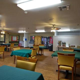 A spacious dining area with green tablecloths and yellow chairs, featuring a beverage station in the background.
