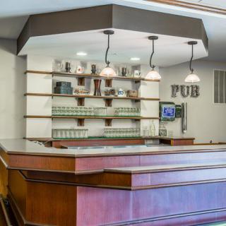 A modern pub interior with a wooden bar counter and shelves stocked with glasses.