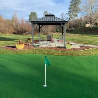 A serene outdoor setting featuring a putting green with a flag and a gazebo in the background.