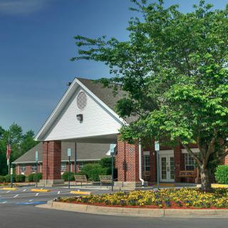 A brick building with a sloped roof surrounded by trees and a landscaped parking lot.