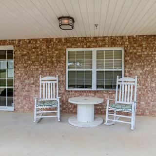 A cozy porch with two white rocking chairs and a small table against a brick wall.