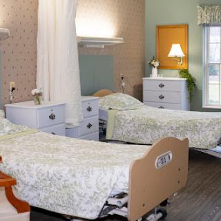 A well-lit patient room featuring two hospital beds, decorated with floral bedding and light-colored walls.