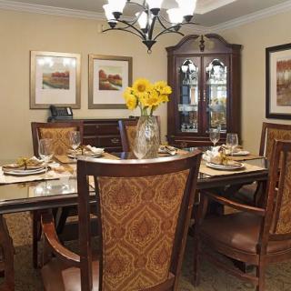 A well-decorated dining room with a central table set, chairs, and a chandelier overhead.