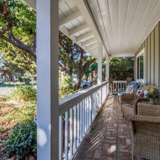 A cozy house porch featuring comfortable seating and surrounded by lush greenery.