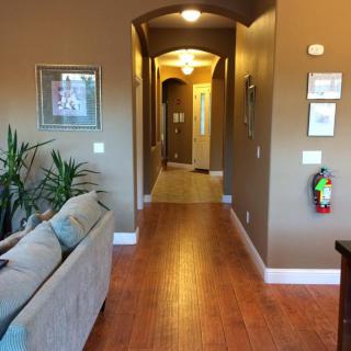 A cozy interior view of a hallway leading from the living room, featuring wooden floors, plants, and artwork on the walls.
