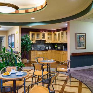 A cozy cafe interior with a small kitchen area, tables and chairs, and decorative plants.