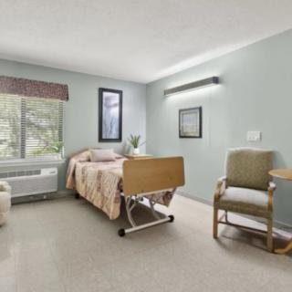 A clean and minimalistic hospital room with a single bed, chair, and large window.