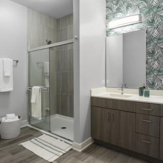 A modern bathroom with a glass shower, vanity sink, and decorative wallpaper.