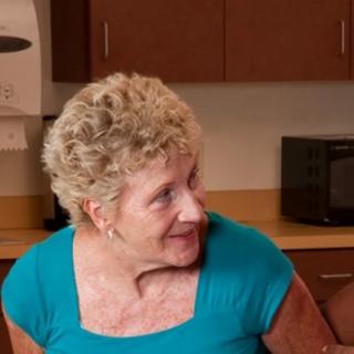 An elderly woman smiling in a kitchen setting.