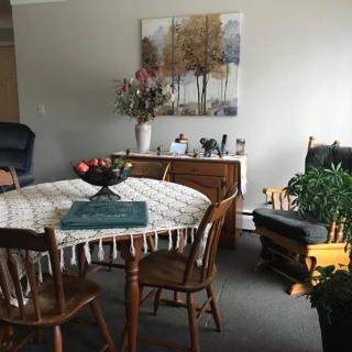 A cozy dining area with a round table, surrounded by wooden chairs, adorned with a tablecloth and centerpiece.