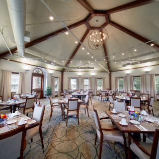 An elegantly designed dining room with neatly arranged tables and chairs, featuring a central chandelier and high ceiling.