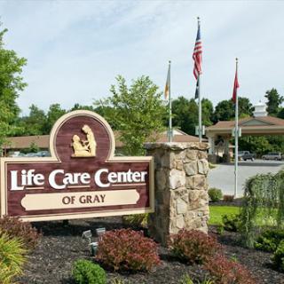 Entrance to the Life Care Center of Gray, featuring well-maintained landscaping and flags.