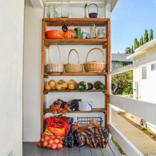 A wooden outdoor shelf stocked with fresh fruits, vegetables, baskets, and jars.