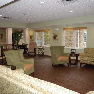 A cozy living room setup with sofas and chairs around tables, featuring large windows and wooden flooring.