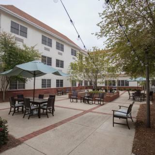 A courtyard with tables, chairs, and umbrellas next to a three-story building.