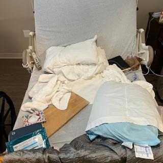 A disheveled hospital bed with various bedding items and medical supplies scattered across it.