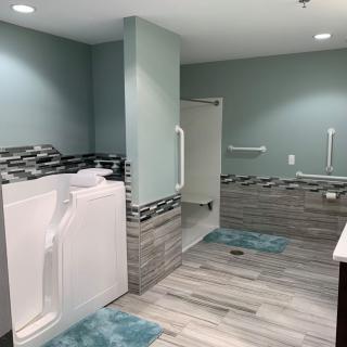 A modern, accessible bathroom with a walk-in tub and shower, featuring tile flooring and grab bars.