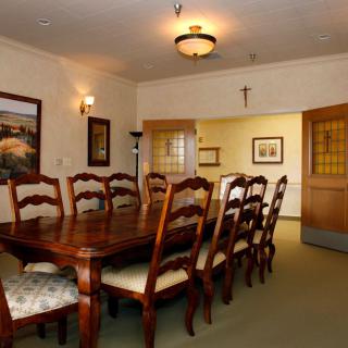 A formal dining room with a large wooden table and chairs, decorated with framed artwork and a ceiling light.