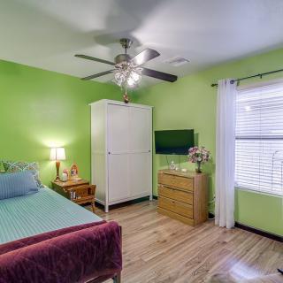 A cozy bedroom with vibrant green walls, featuring a bed, a wardrobe, and a dresser, illuminated by natural light through a window.
