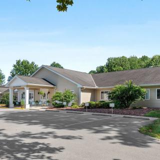 A single-story building with a driveway and surrounding greenery under a clear blue sky.