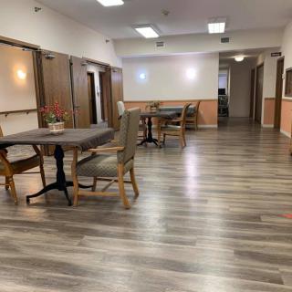 A spacious dining area with wooden flooring, featuring several tables and chairs under bright lighting.