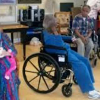A group of elderly individuals seated together in a care facility, with some using wheelchairs.