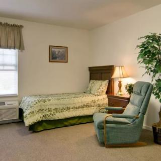 A cozy bedroom with a single bed, upholstered chair, and a potted plant near the window.