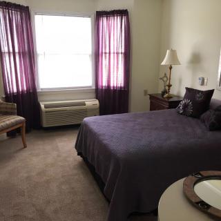 A cozy bedroom with a bed, lamp, and window with purple curtains.