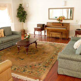 A cozy living room with sofas, a piano, and a coffee table, adorned with a large rug and decorative plants.