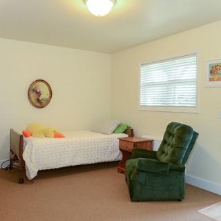 A simple bedroom with a single bed, green upholstered chair, and wall art.