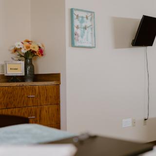 A serene hospital room featuring a bedside table with flowers, artwork on the wall, and a television.