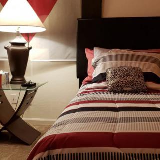 A cozy bedroom setting featuring a bed with striped bedding and a modern lamp on a nightstand.