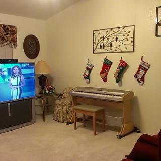 A cozy living room with a TV, piano, and Christmas stockings hung on the wall.