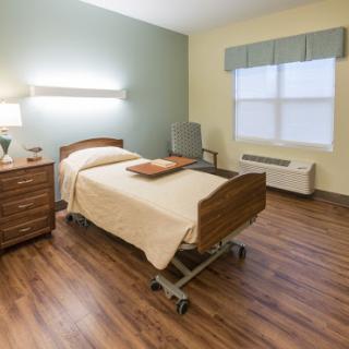 A well-lit hospital room featuring a neatly made bed, bedside table, and a large window.