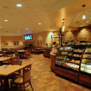 A cozy cafe interior featuring a display case filled with pastries and arranged tables and chairs.