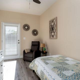 A minimalist bedroom featuring a bed with a patterned quilt, an armchair, wall decor, and abundant natural light.