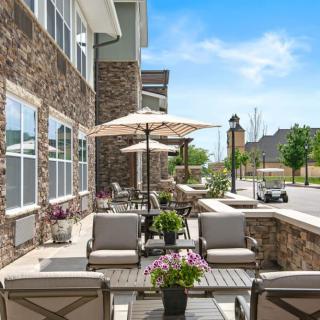 A cozy outdoor patio area with seating and umbrellas on a sunny day, adjacent to a stone building.
