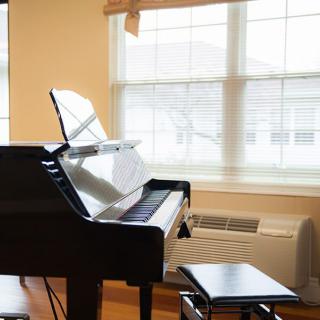 A sunlit room with a grand piano and stool by the window.