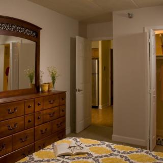 A cozy bedroom with a wooden dresser and a mirror, featuring a patterned bedspread and open doorways.