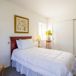 A cozy bedroom with a neatly made bed, white bedding, a lamp, and floral decor.