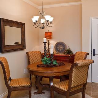 A cozy dining room with a round table and four upholstered chairs, adorned with a chandelier and decorative items on the sideboard.