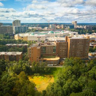 A scenic view of a city skyline with prominent buildings and lush greenery under a partly cloudy sky.