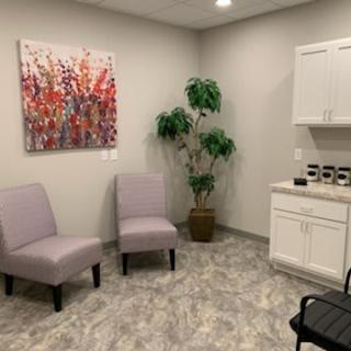 A quiet waiting room with two chairs, a vibrant painting, and a potted plant.