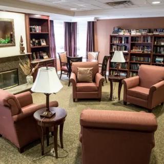 A cozy library seating area with armchairs, lamps, and bookshelves.